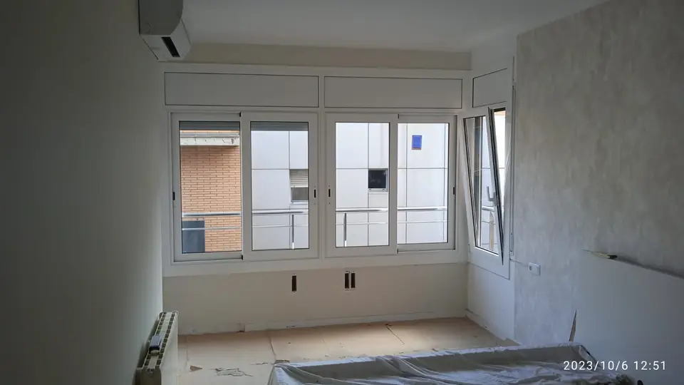 Salón con ventanas correderas y practicable de aluminio blanco recién instaladas, con el suelo protegido