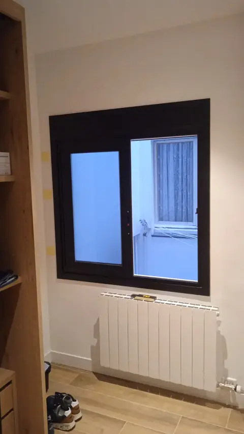 Ventana corredera de aluminio negro con una hoja de vidrio translúcido en un dormitorio