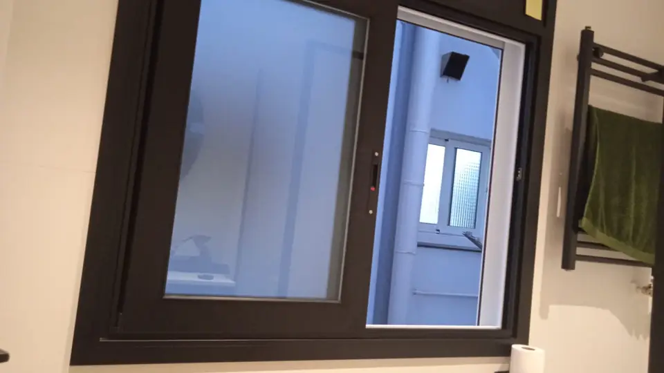 Ventana corredera de aluminio negro en un baño, con vidrio translúcido